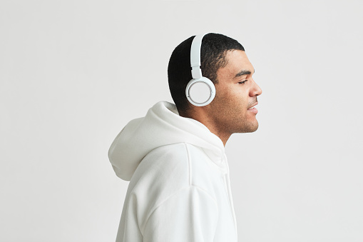 Minimal side view portrait of modern Latin American man wearing headphones white hoodie while listening to music, copy space