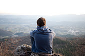 Young man looking at the view and sitting on a rock. Copyspace above the horizon.