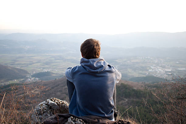 Young man looking at the view, copyspace Young man looking at the view and sitting on a rock. Copyspace above the horizon. staring stock pictures, royalty-free photos & images