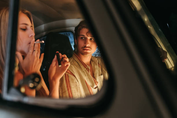 un jeune homme regardant une femme fumer de la marijuana dans une voiture - cannabis voiture jeune photos et images de collection