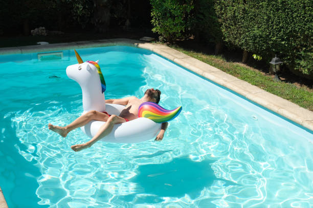 Young man on a big unicorn inflatable ring in a swimming pool. Summer concept. stock photo