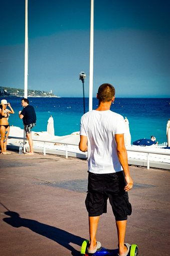 Nice, France - July 29, 2015: A young man on a hoverboard on the Promenade des Anglais in Nice, France with other tourists in the background.