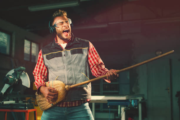 Young man on break at work has a headphones and holds a broom in his hands and pretending to play the guitar stock photo