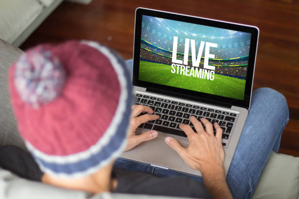 Young man on the sofa live streaming Young man watching live streaming sports event. All screen graphics are made up. streaming service stock pictures, royalty-free photos & images
