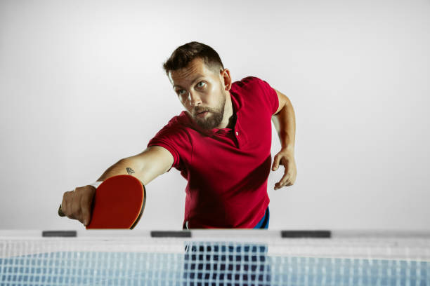 Goal. Young man plays table tennis on white studio background. Model...