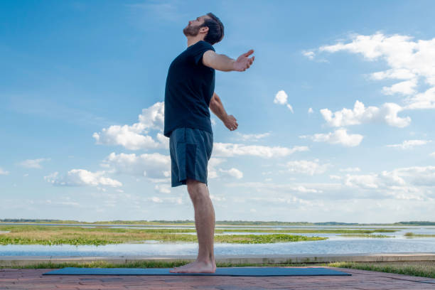 A young man practices yoga in front of a lake stock photo