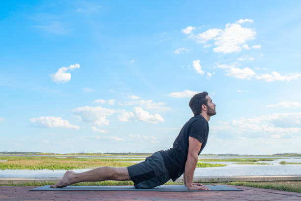 A young man practices yoga in front of a lake stock photo