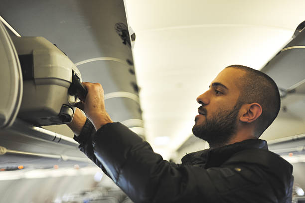 Young man putting a suitcase in an overhead compartment stock photo