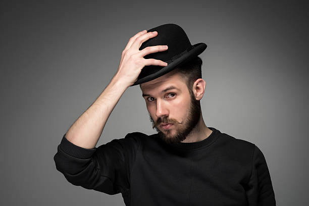 Young man raising his hat  in respect and admiration for Young man with a mustache and beard raising his hat  in respect and admiration for someone. portrait on gray background.  hats off to you stock pictures, royalty-free photos & images