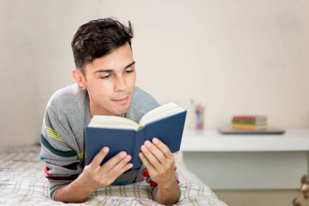 young man reading a book in his bedroom. Resting stock photo