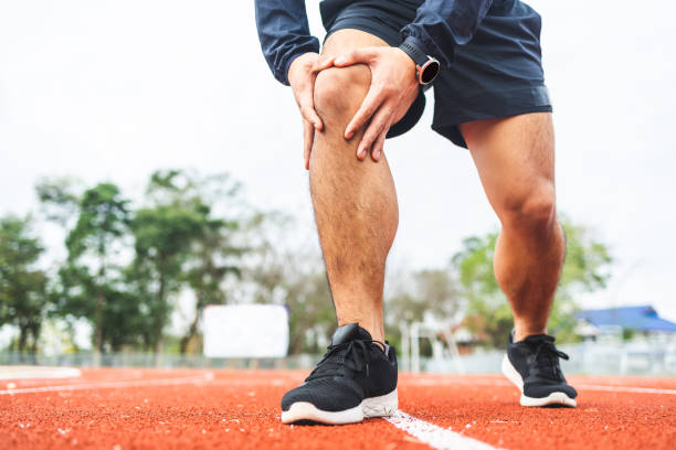 Young man runner has sore knee because he ran too long. Male Exercising until the injury. Overtrained. Young sport man accident running on track stock photo