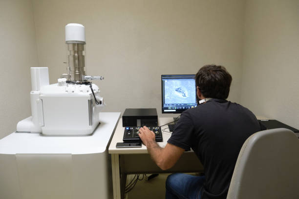 Young man scientist working with scanning electron microscope. Laboratory technician observing samples with a SEM. Young man scientist working with scanning electron microscope. Laboratory technician observing samples with a SEM. electron microscope stock pictures, royalty-free photos & images