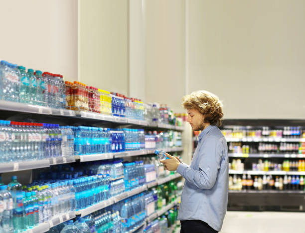 jonge mens die in supermarkt winkelt, die een fles water in een supermarkt koopt - soda supermarket stockfoto's en -beelden