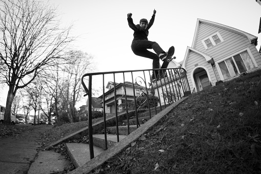 Young man board sliding down a hand rail infront a residential house in Portland, Oregon.