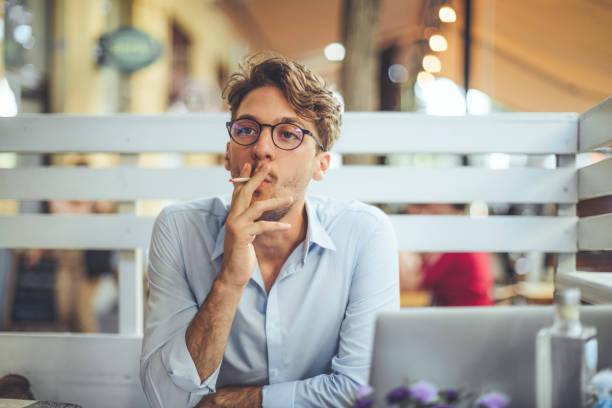 Young man smoking a cigarette in a sidewalk cafe stock photo