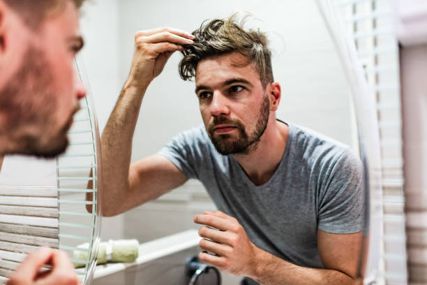 jeune homme stylisant ses cheveux dans la salle de bains - homme miroir photos et images de collection