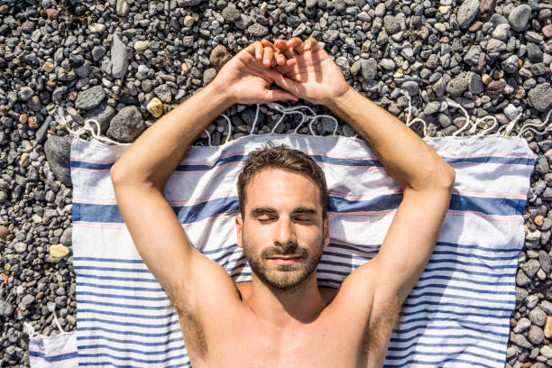 Young man sunbathing on a beach of stones stock photo