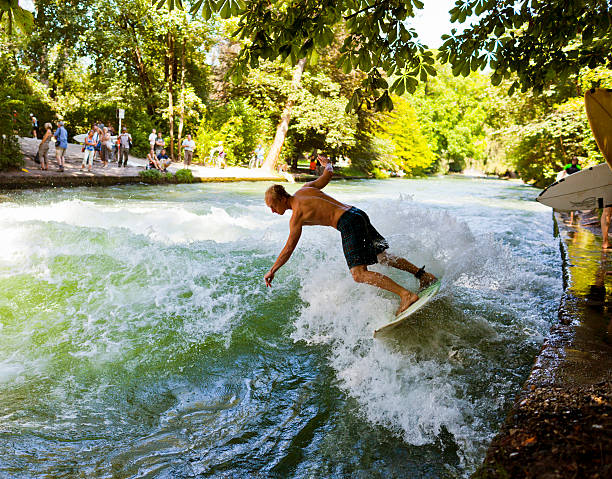 Young man surfing at the Eisbach river in Munich Germany Munich, Germany - August 26, 2011: Man surfing with other people watching at the Eisbach river in Munich Germany. The Eisbach river is a small but fast and cold stream of water tributary of the Isar river that flows through the Englischer Garten park where surfers gather to practise their sport specially at this spot were the river forms a standing wave river isar stock pictures, royalty-free photos & images