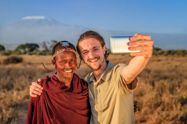 Young man taking selfie with warrior Maasai, Mount Kilimanjaro on background, Kenya, Africa Young male tourist taking selfie with a warrior from Maasai tribe, Mount Kilimanjaro on background, Southern Kenya, Africa. Maasai tribe inhabiting southern Kenya and northern Tanzania, and they are related to the Samburu. mt kilimanjaro photos stock pictures, royalty-free photos & images