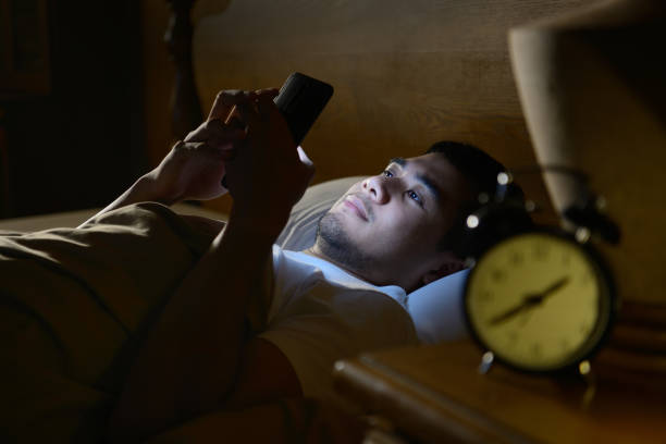 Young man using a smartphone in his bed at night stock photo