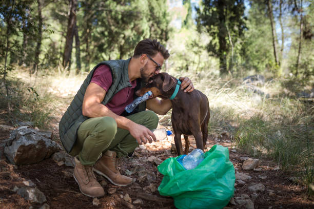 Young man volunteer and his dog cleaning forest from plastic waste and preserving ecology stock photo