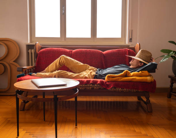 Young man wearing a hat sleeping on the sofa waiting for inspiration, lazy boy rests during break to recharge his energy stock photo
