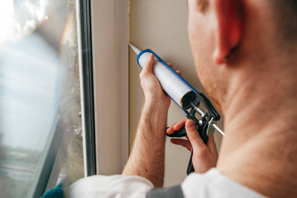 Young man wearing overalls sealing cracks between window and trim Young man wearing overalls sealing cracks between window and trim using waterproof silicone caulk on the balcony. seal crack caulk stock pictures, royalty-free photos & images