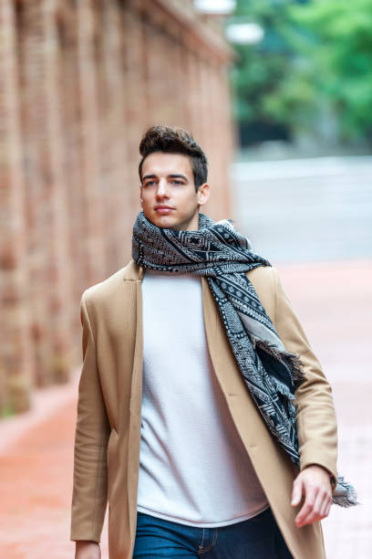 Young man wearing winter clothes in the street. Young guy with modern hairstyle with coat, blue jeans and white sweeter. stock photo