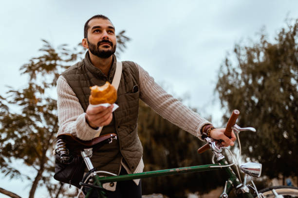 Young man with a bicycle eating breakfast in the park stock photo