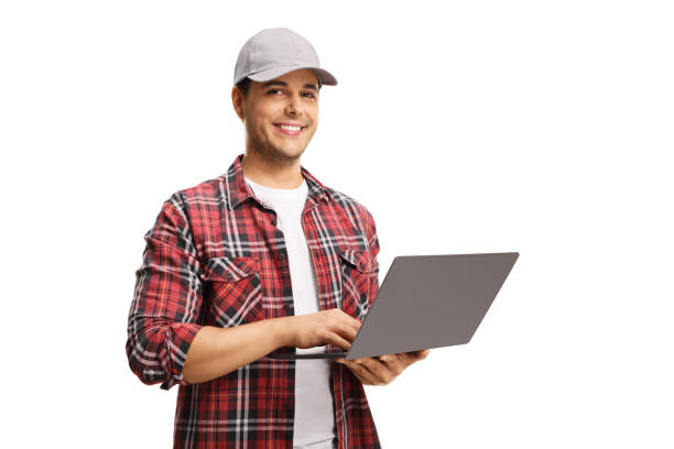 Young man with a cap holding a laptop computer and smiling at the camera Young man with a cap holding a laptop computer and smiling at the camera isolated on white background cap hat stock pictures, royalty-free photos & images