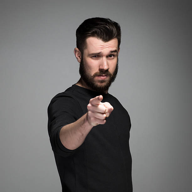 Young man with beard and mustaches, finger pointing towards the Young man with beard and mustaches, finger pointing towards the camera on a gray background desire stock pictures, royalty-free photos & images