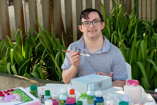 happy young man with down syndrome smiling and making handicraft outdoors