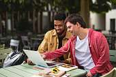 istock Young man with Down syndrome with his mentoring friend sitting outdoors in cafe using laptop. 1347212805
