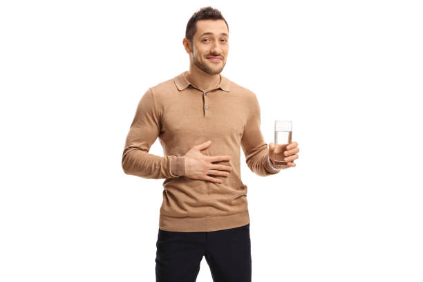 Young man with glass of water holding hand on stomach Young man with a glass of water holding his hand on his stomach isolated on white background drinking water digestion stock pictures, royalty-free photos & images