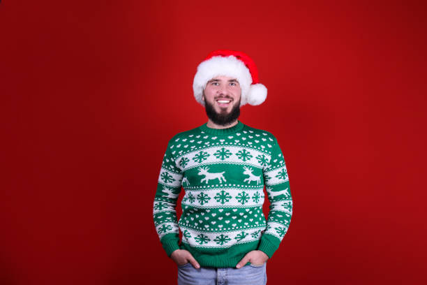 Young man with perfectly groomed beard in Christmas outfit on red wall background. Studio portrait of handsome bearded man wearing christmas sweater with snowflake ornament, posing over the red wall, copy space for text. Festive background. Male with facial hair smiling. ugliness stock pictures, royalty-free photos & images