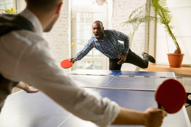 Young men playing table tennis in workplace, having fun. Friends in...
