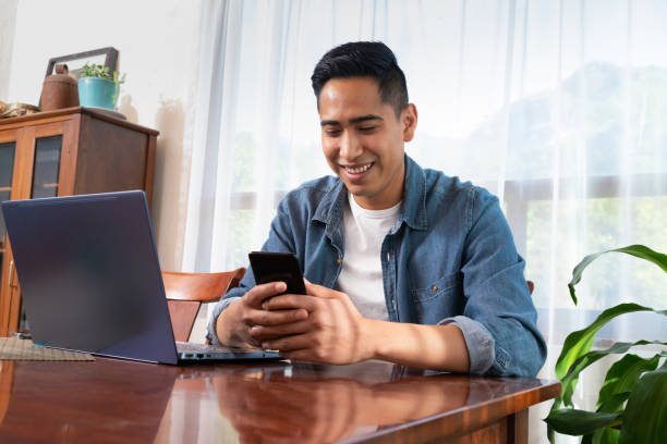 Young mexican latinx man using laptop and smartphone stock photo