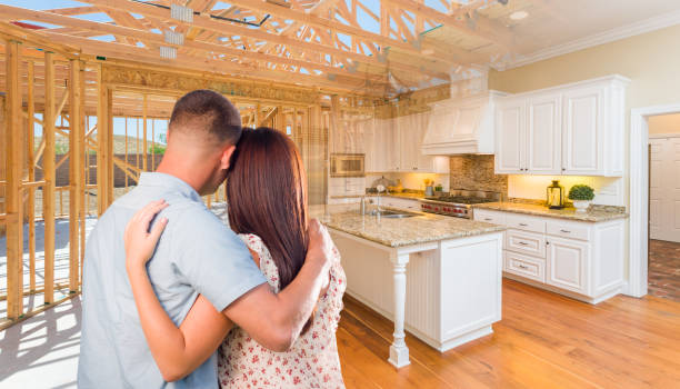 Young Military Couple Facing House Construction Framing Gradating Into Finished Kitchen Build stock photo