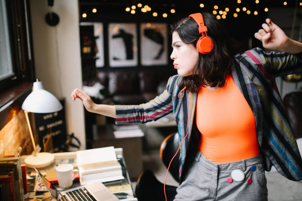 young millennial dancing to the music in her Downtown Los Angeles apartment Young Latinx woman sitting at the desk in her Los Angeles apartment, receiving happy news over the social networks or just having a nice day, dancing to the music. hipster culture photos stock pictures, royalty-free photos & images