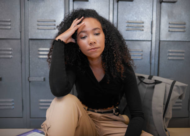 A young mixed race woman sits in front of school lockers looking depressed stock photo