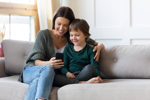 Young mom and small son relax at home with smartphone stock photo