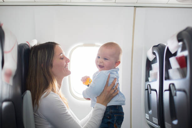 Young mom, playing and breastfeeding her toddler boy on board of aircraft stock photo