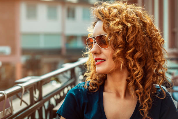 young moroccan woman, with curly brown hair, sitting in an outdoor cafe in Mainz, wearing sunglasses stock photo