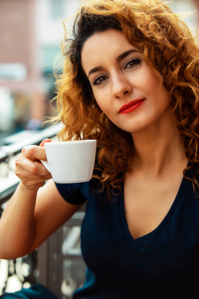young moroccan woman, with curly brown hair, sitting in an outdoor cafe in Mainz, drinking coffee stock photo