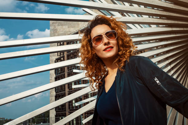 young moroccan woman with curly hair, wearing sunglasses, turning to camera, in an urban environment stock photo