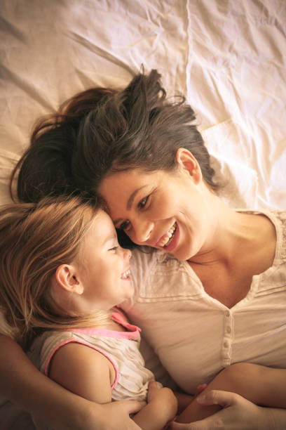 Young  mother and daughter laying in bed together at home. stock photo