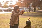 若い母親と息子が公共の公園で落ち葉で遊んで