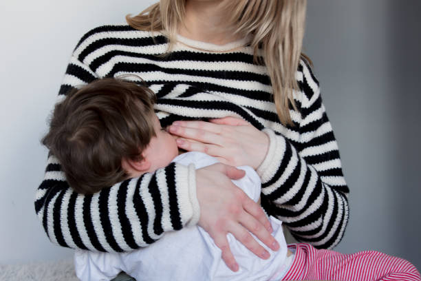 Young mother breastfeeding toddler boy in striped sweater stock photo