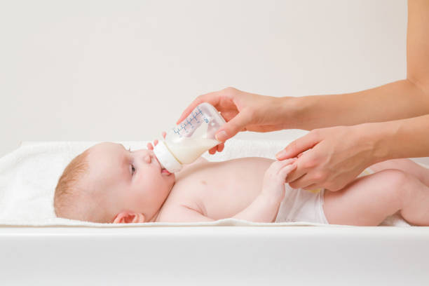 madre joven alimentando al bebé con biberón de leche. bebé en la mesa de cambio. closeup. vista lateral. - baby formula fotografías e imágenes de stock