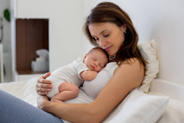 Young mother lying in bed with her newborn baby boy stock photo